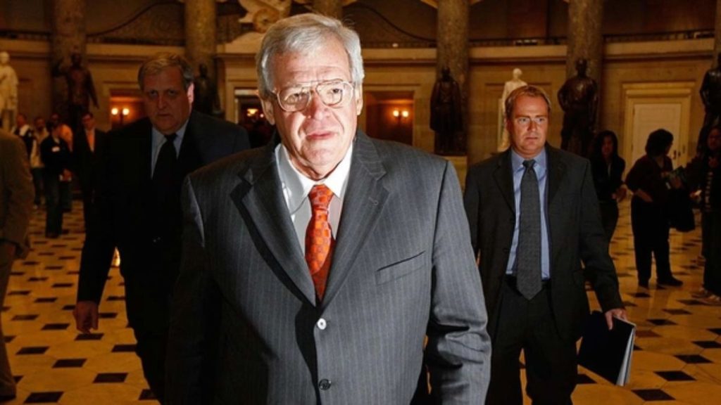 Dennis Hastert wearing a suit and walking through a government building